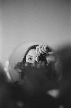 Black and white photo of a woman taking a mirror selfie with a camera, showcasing reflection artistry.