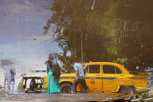 Free A reflection of a yellow taxi and pedestrians on a rainy Kolkata street. Urban life captured. Stock Photo