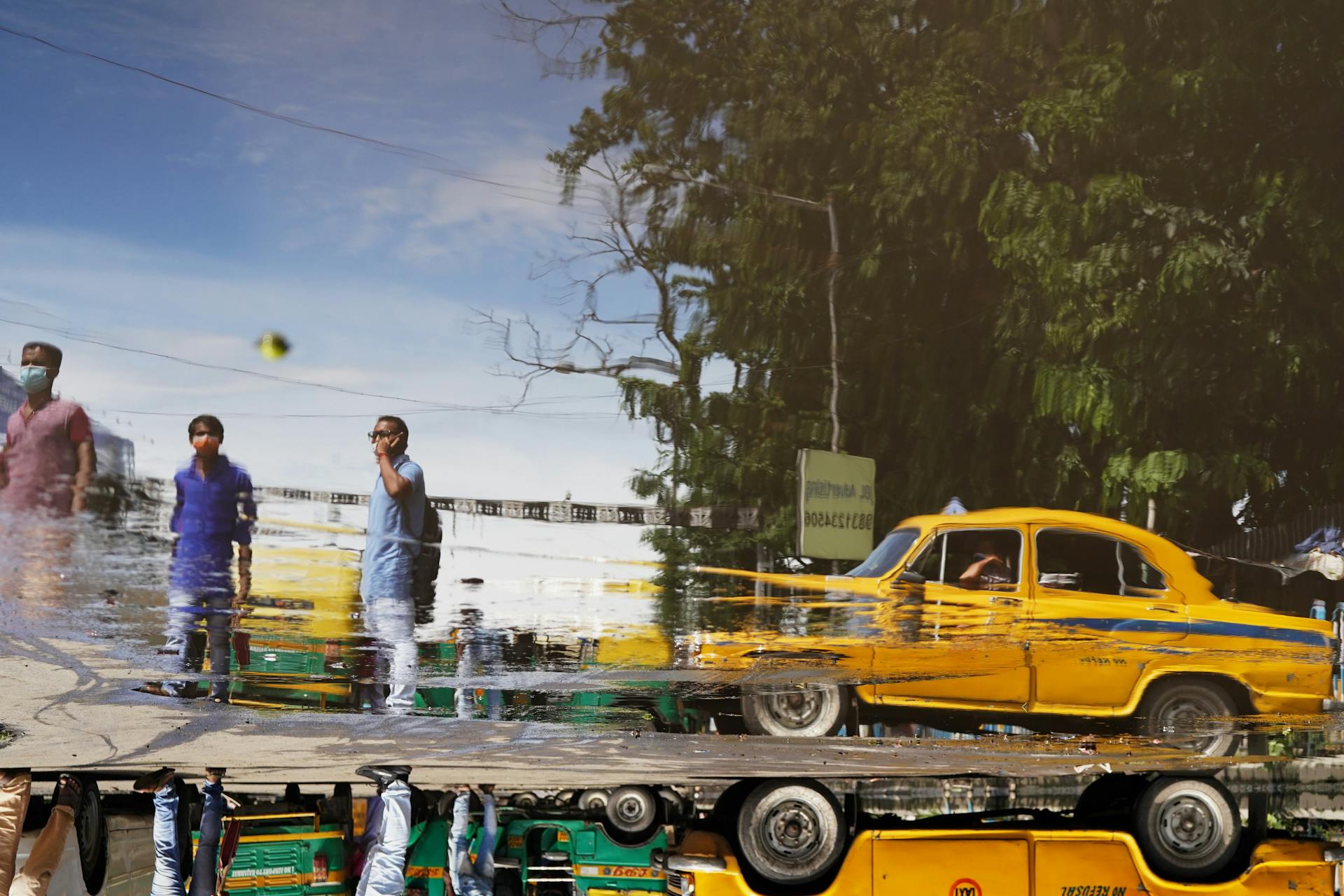 Reflection of people and an Ambassador taxi in a water puddle on a Kolkata street.