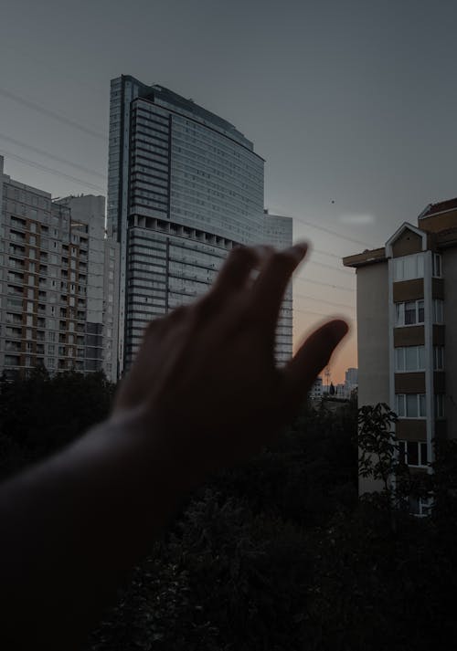 A person's hand reaching out to the sky with a city in the background