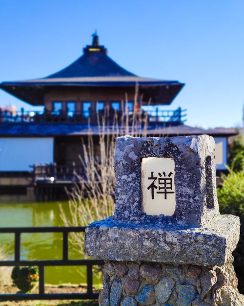 Free A peaceful Buddhist temple near a pond with a prominent Zen symbol on a stone pillar. Stock Photo