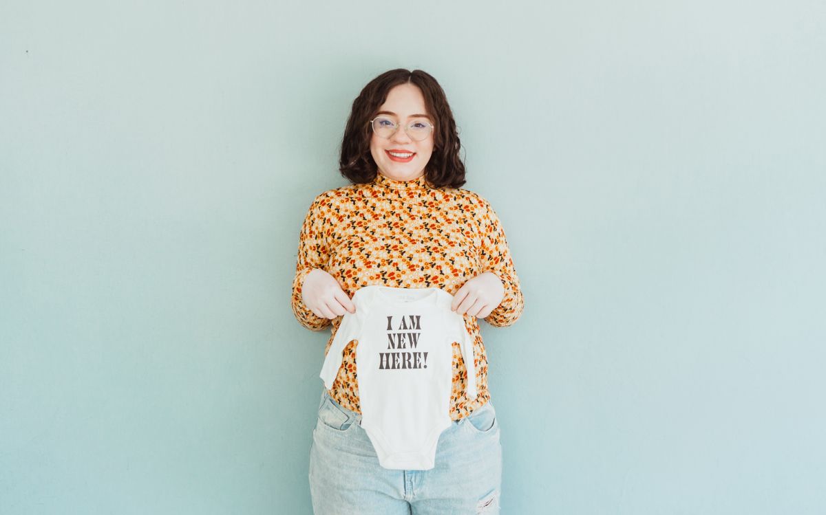 Baby shower photo booth ideas with a woman holding a baby onesie that says I am new here