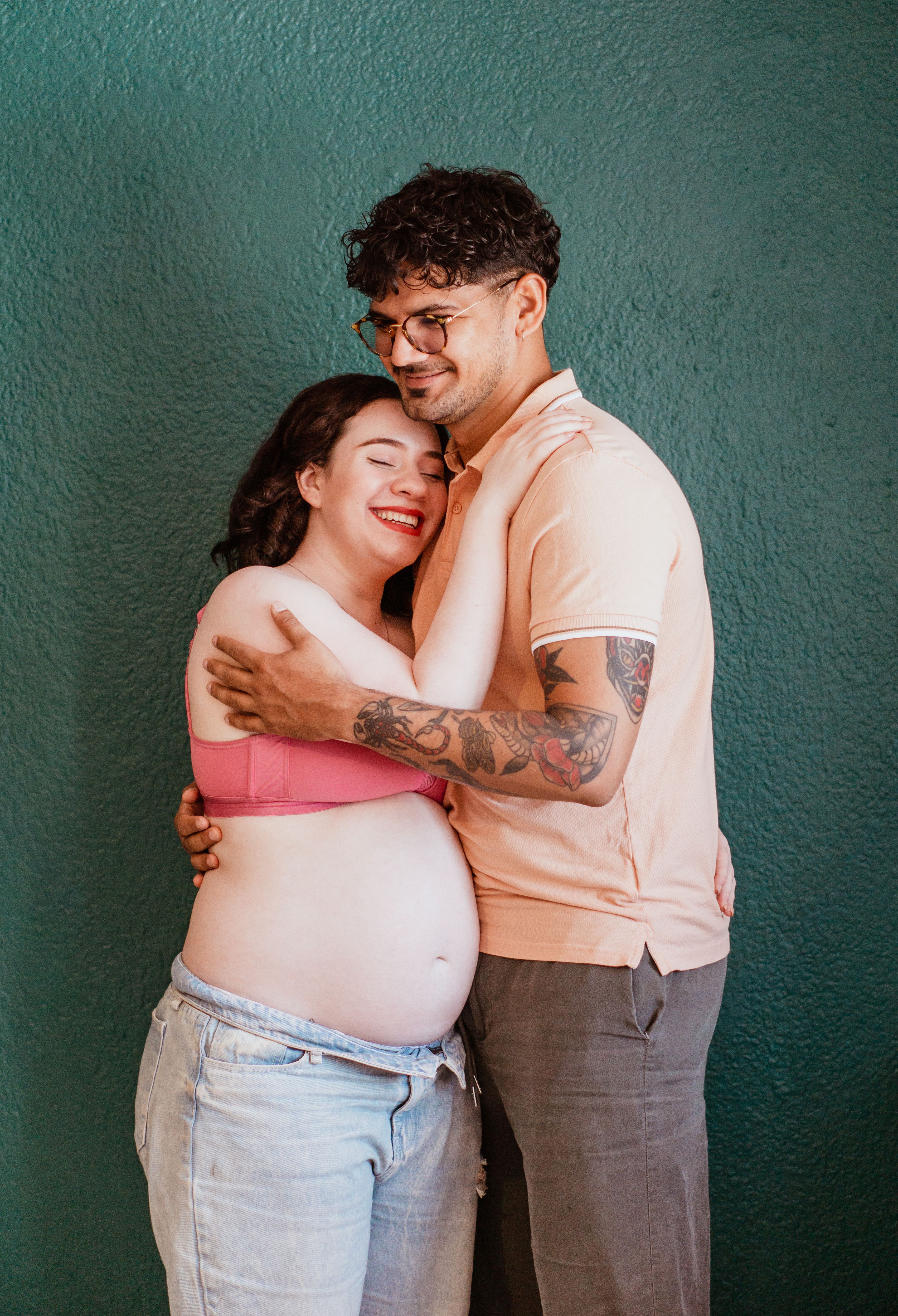 Fotomural Una pareja embarazada alegre se abraza tiernamente contra un fondo verde vibrante en interiores.