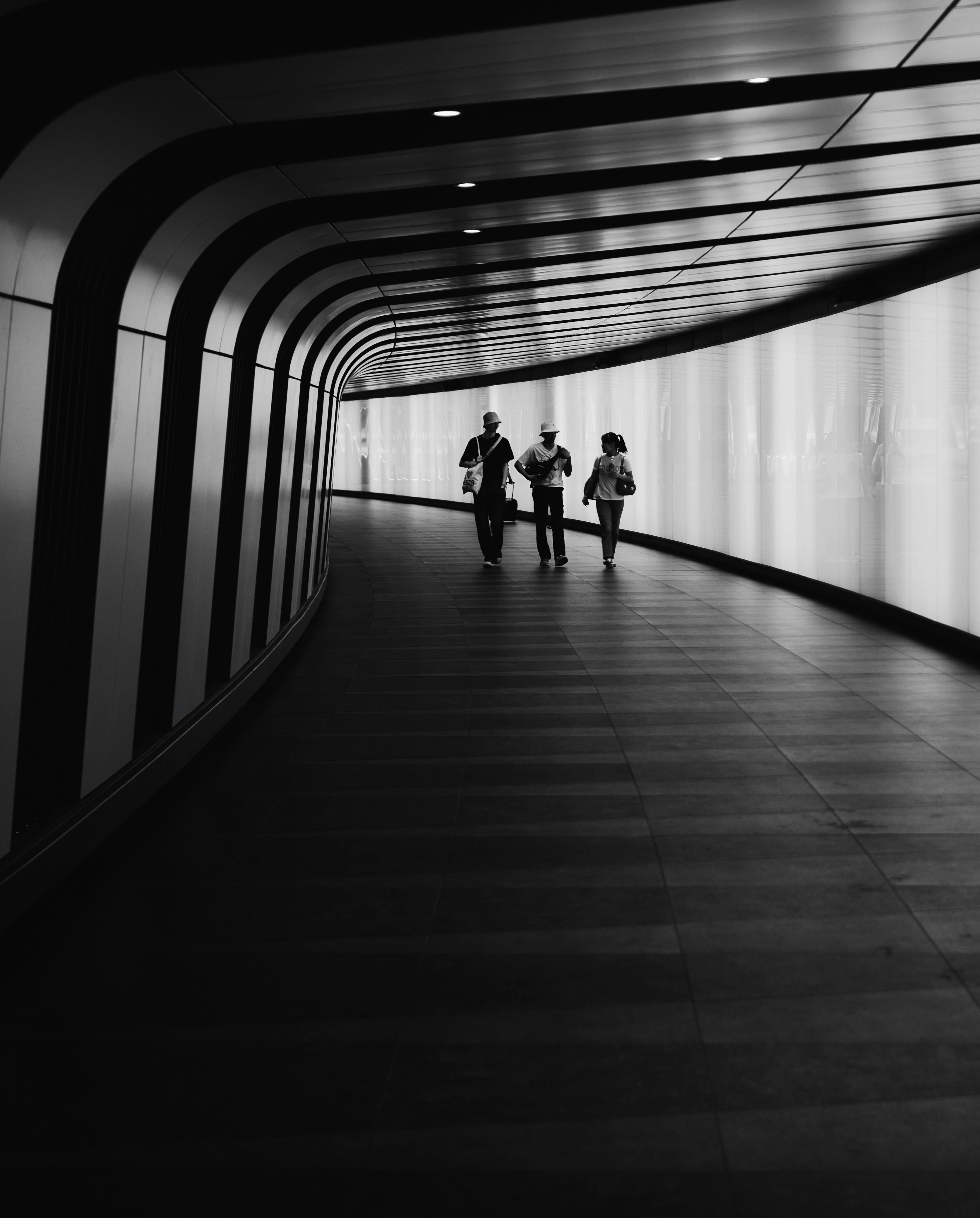 Three people walk in a futuristic black and white tunnel with high contrast lighting.