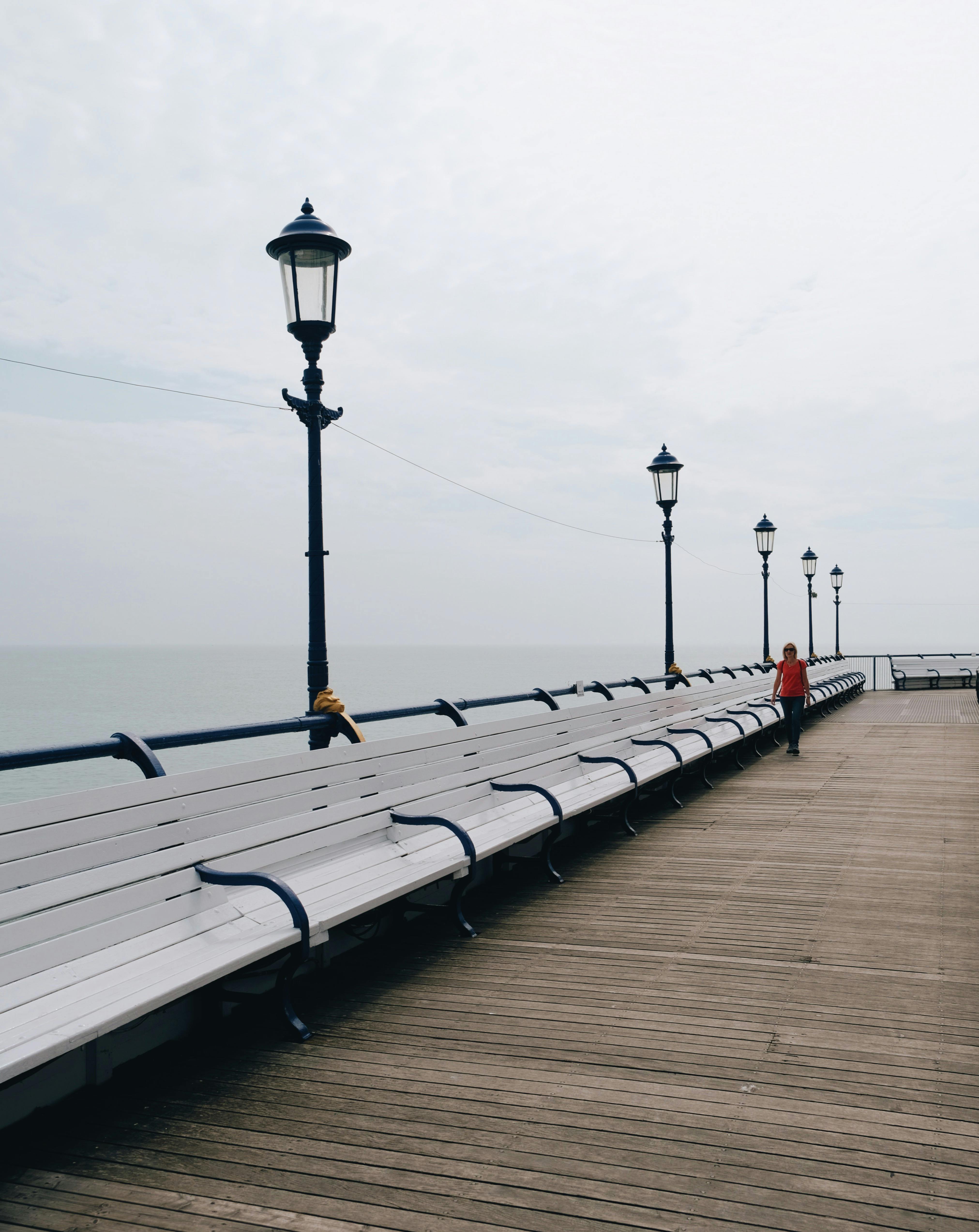 A peaceful walk on a seaside pier lined with classic lamp posts and benches.