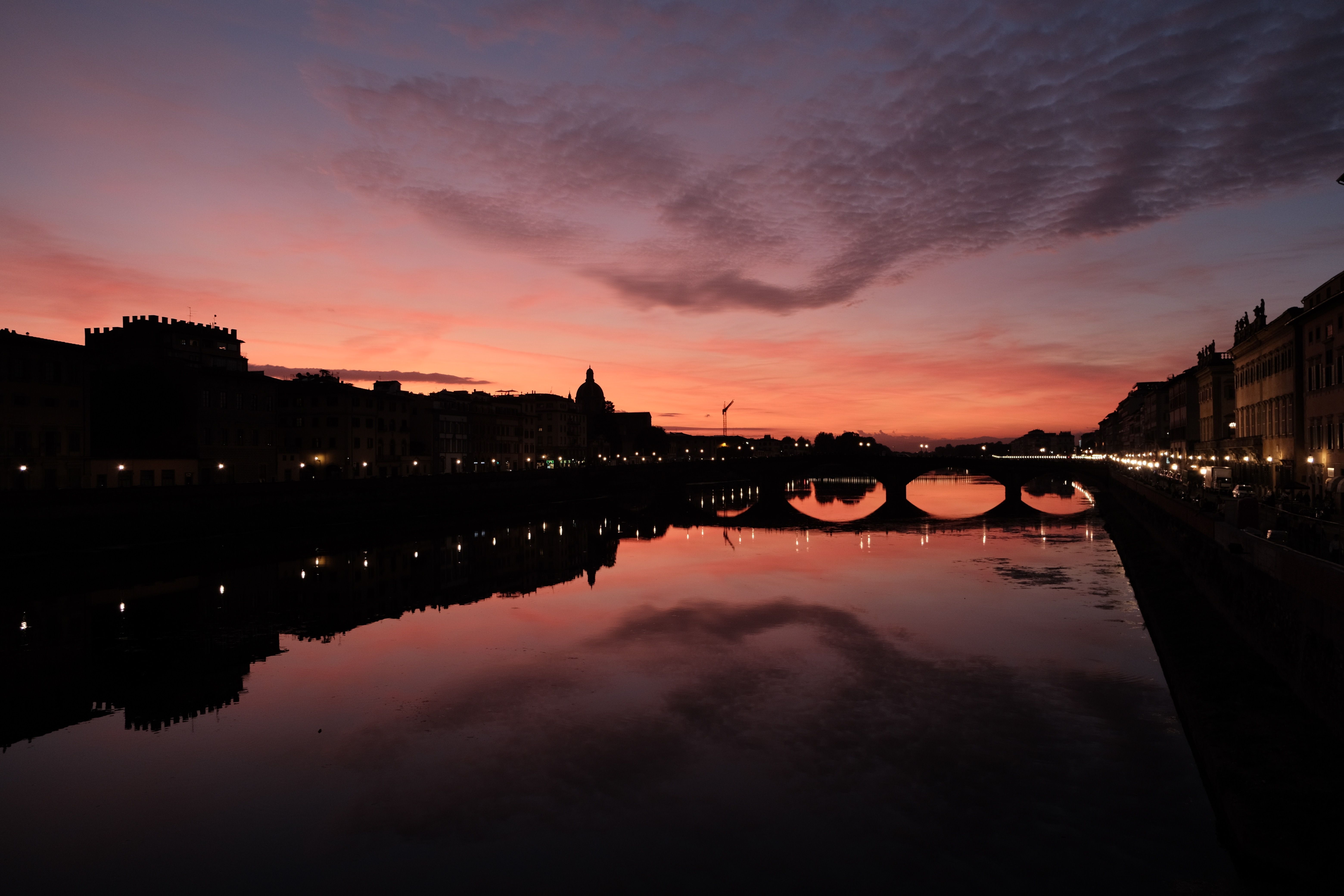 Beautiful sunset view of Ponte Vecchio in Florence, Italy, reflecting in the Arno River.