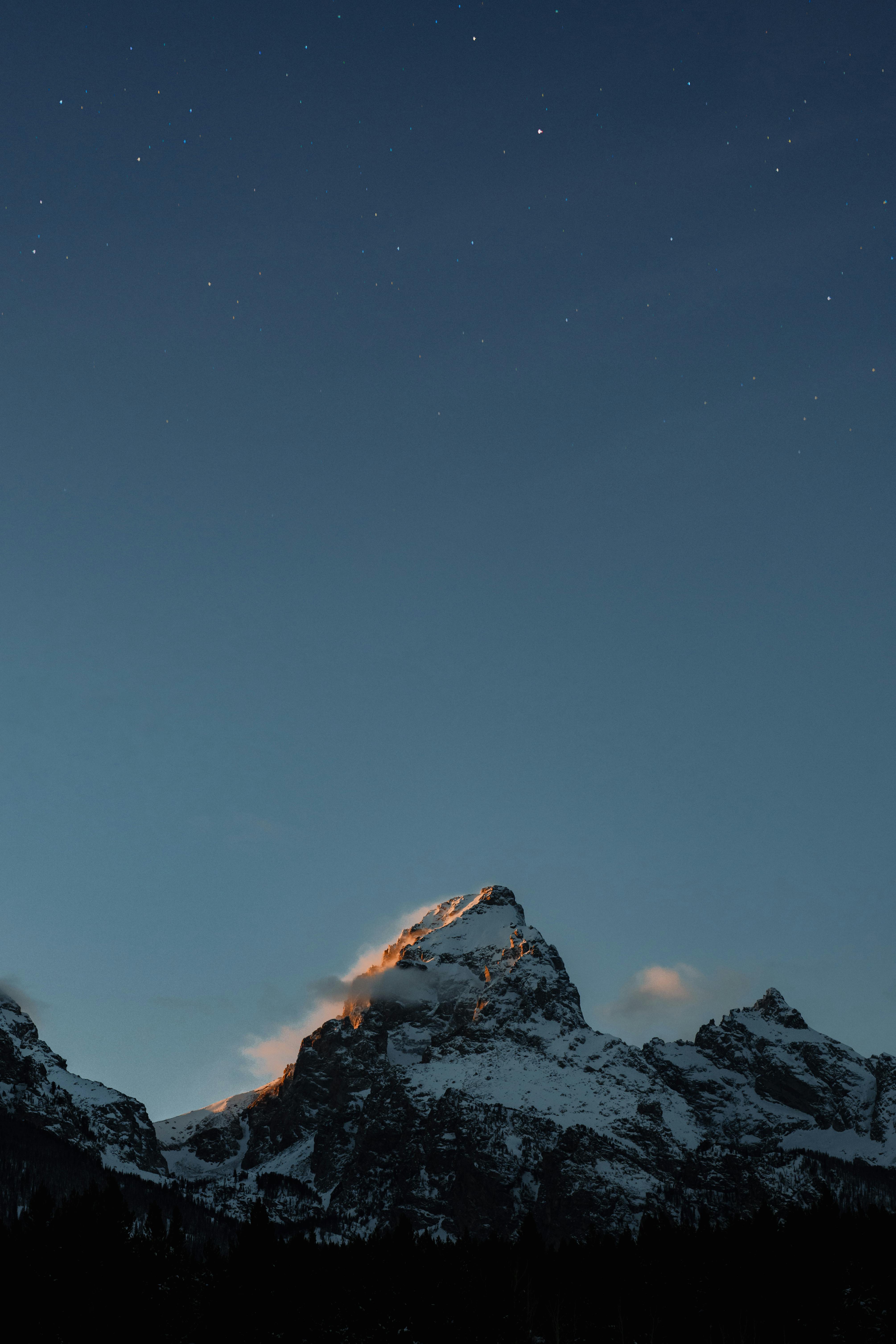 A breathtaking view of a snowy mountain peak under a starry evening sky, perfect for scenic mobile wallpapers.