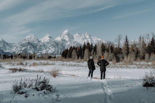 Two people walking through the snow in front of the grand teton mountains