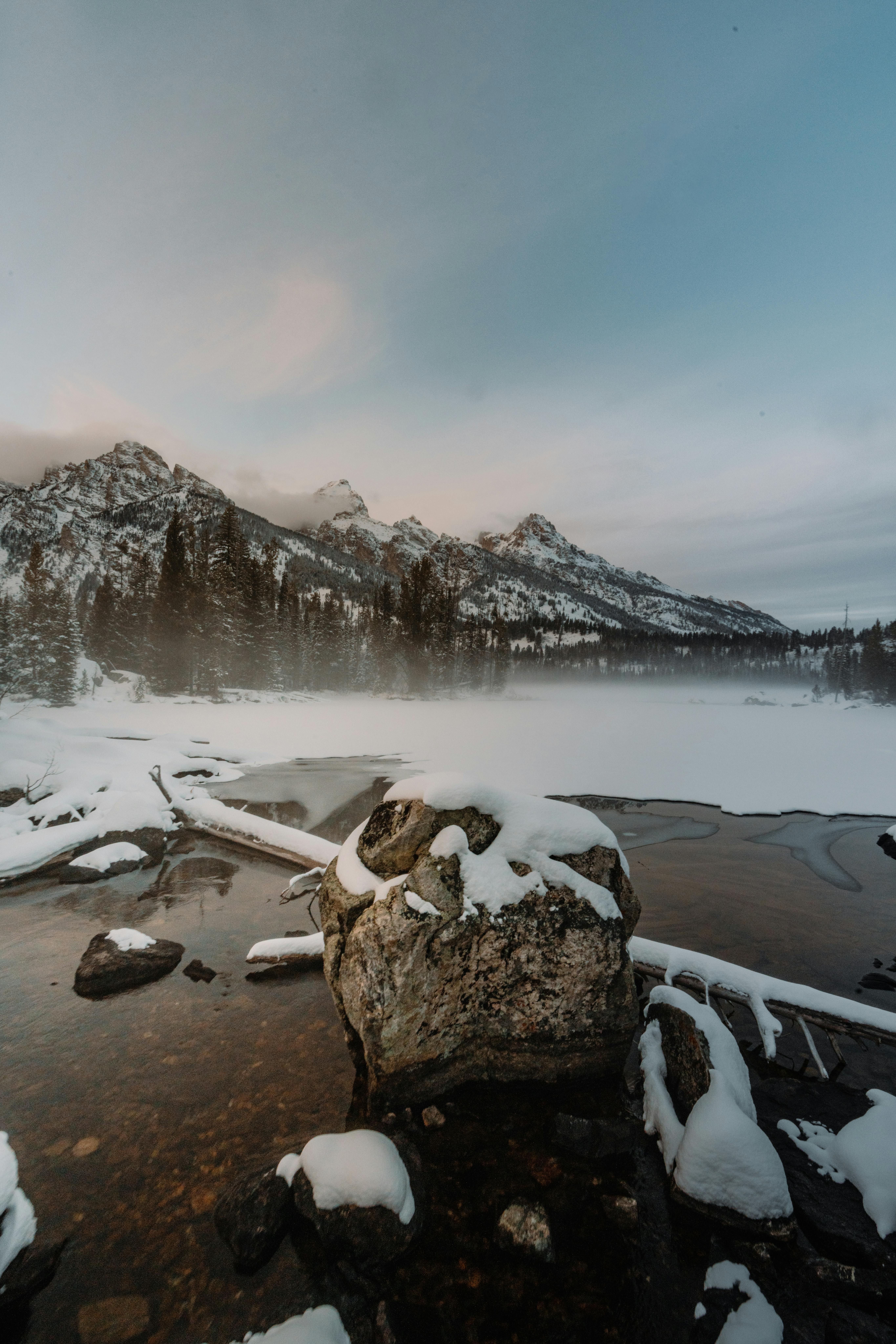 Serene winter landscape with snow-covered mountains and a peaceful lake reflecting the scenery.