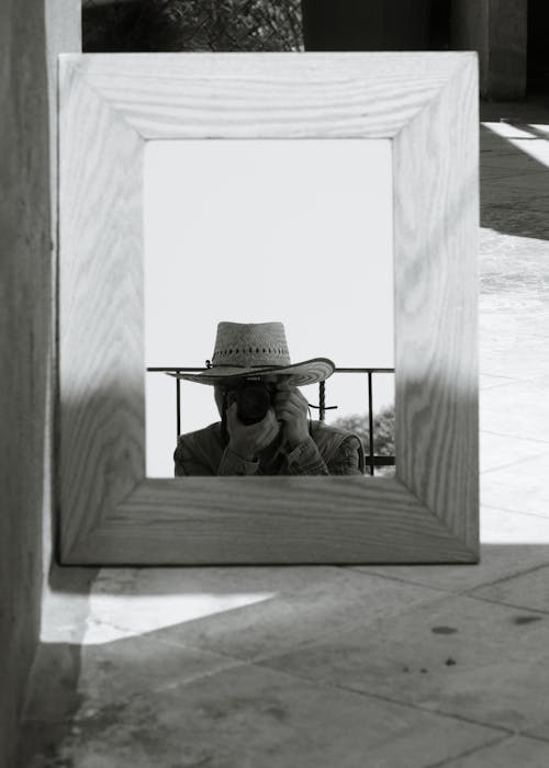 A man in a hat taking a picture of himself in a mirror