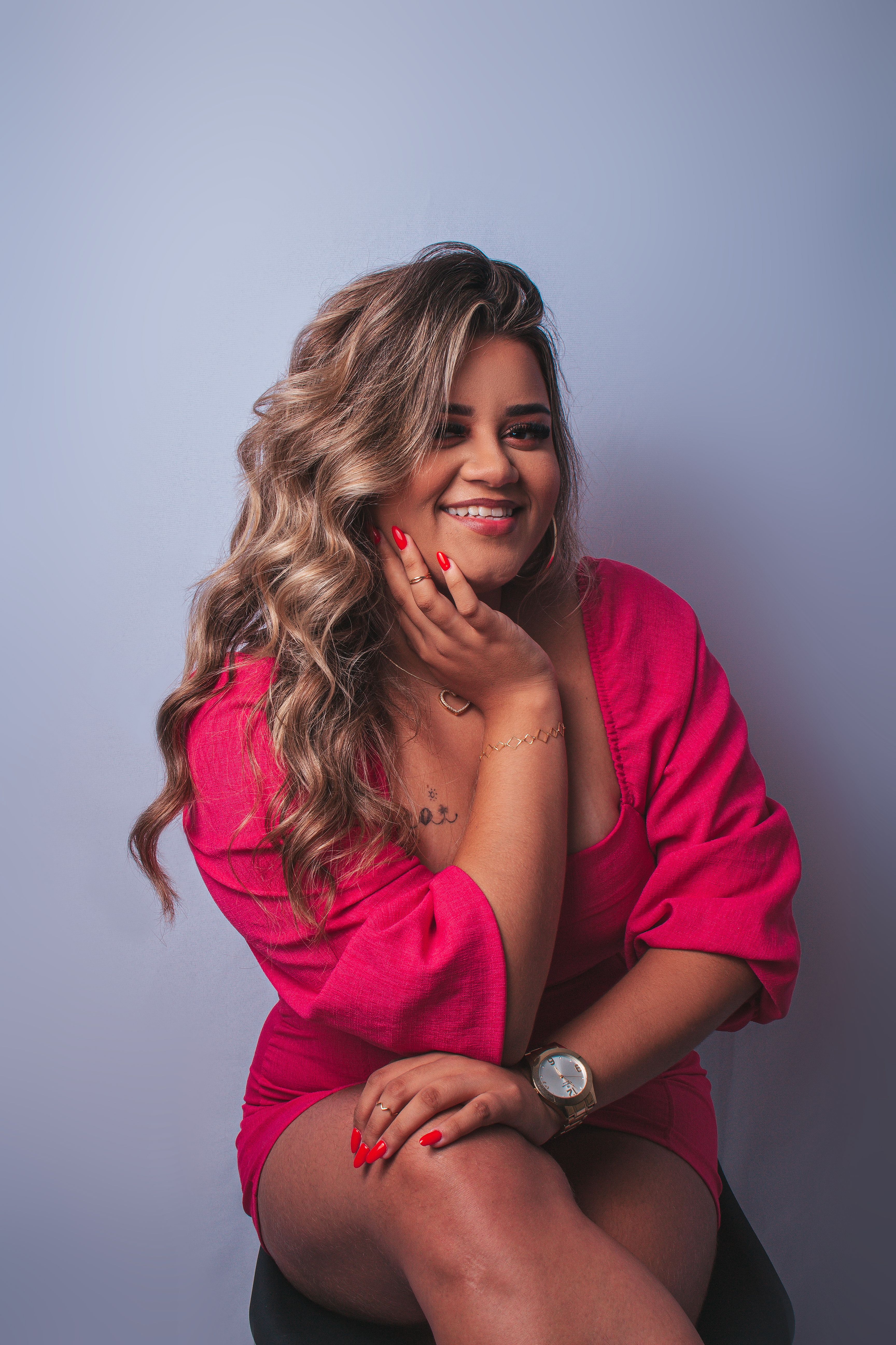 Portrait of a smiling woman in a vibrant pink dress posing indoors against a neutral background.