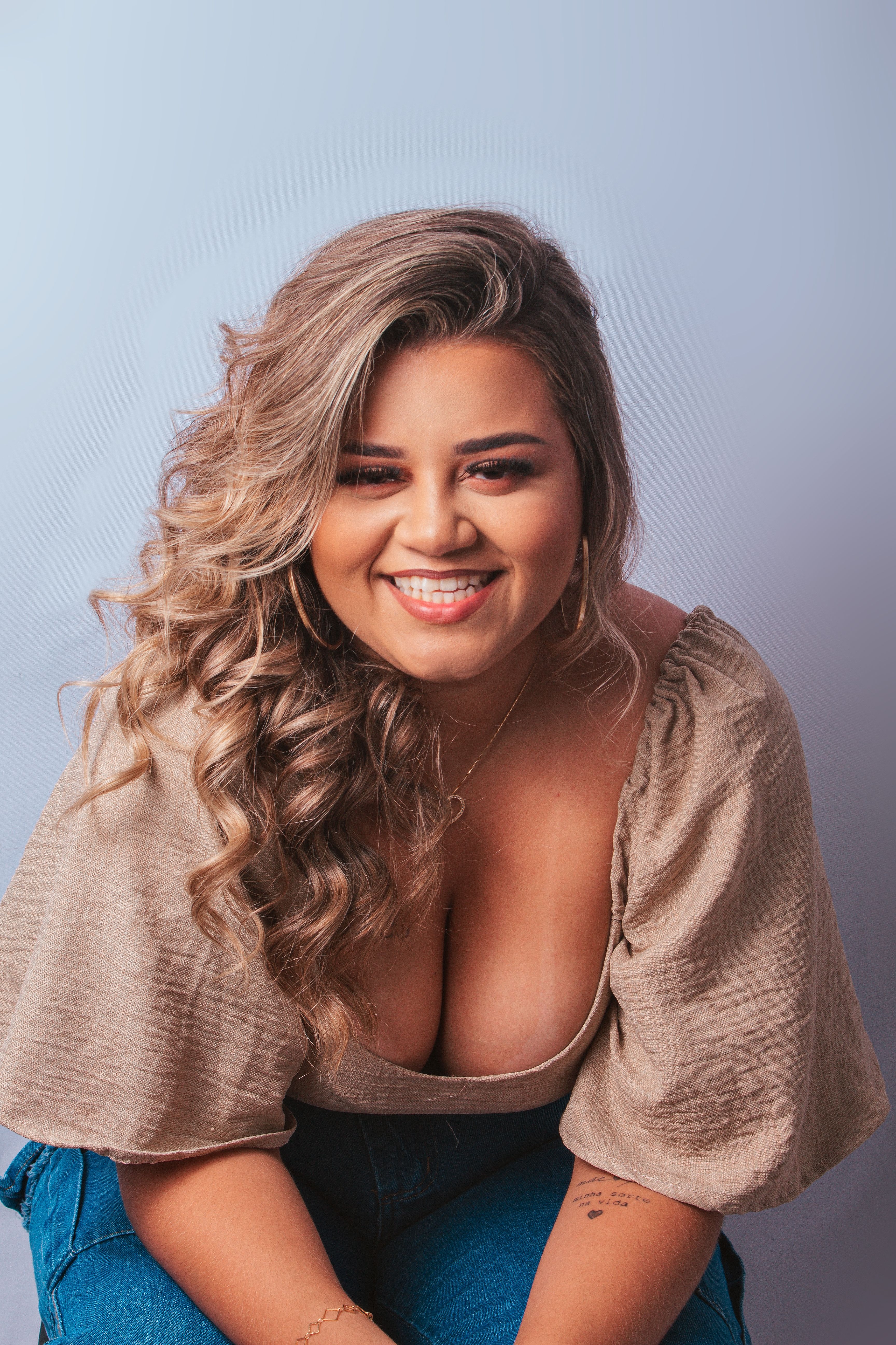 Portrait of a smiling young woman with curly blonde hair, wearing casual attire in a studio.