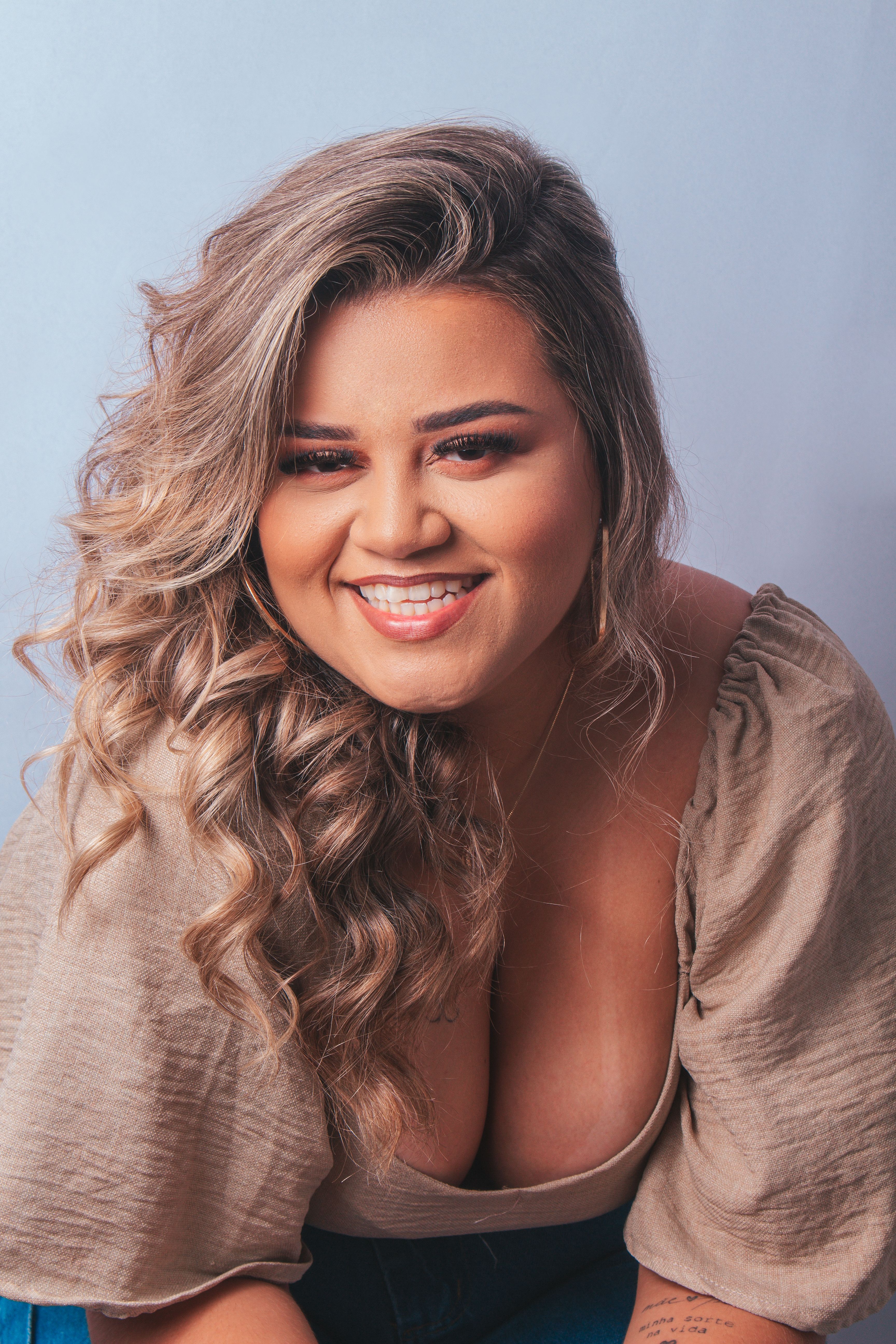 Joyful woman with blonde curls in a studio setting, showcasing fashion and confidence.