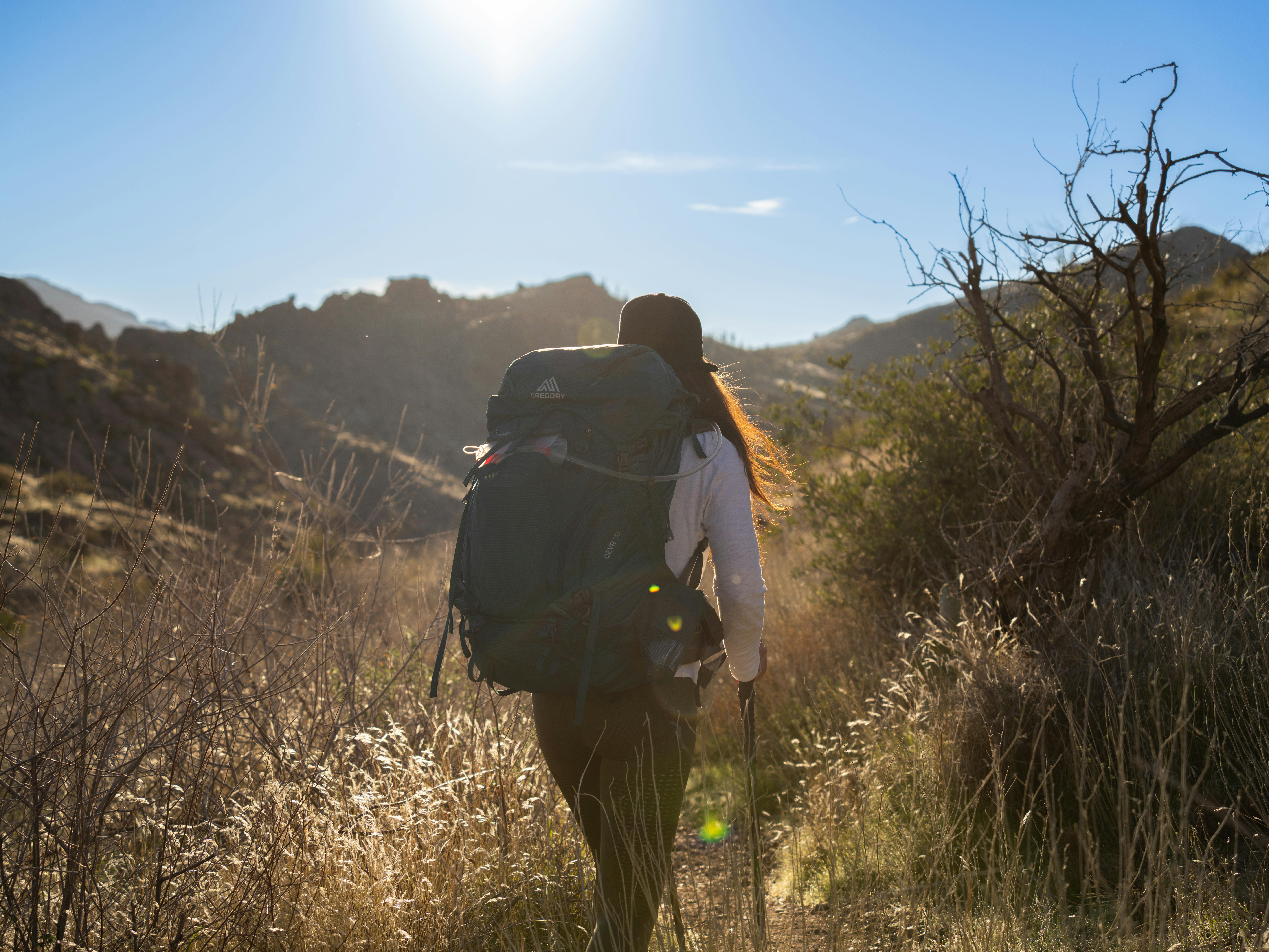 Backpack-wearing woman hikes through Superstition Mountains, AZ under the morning sun.