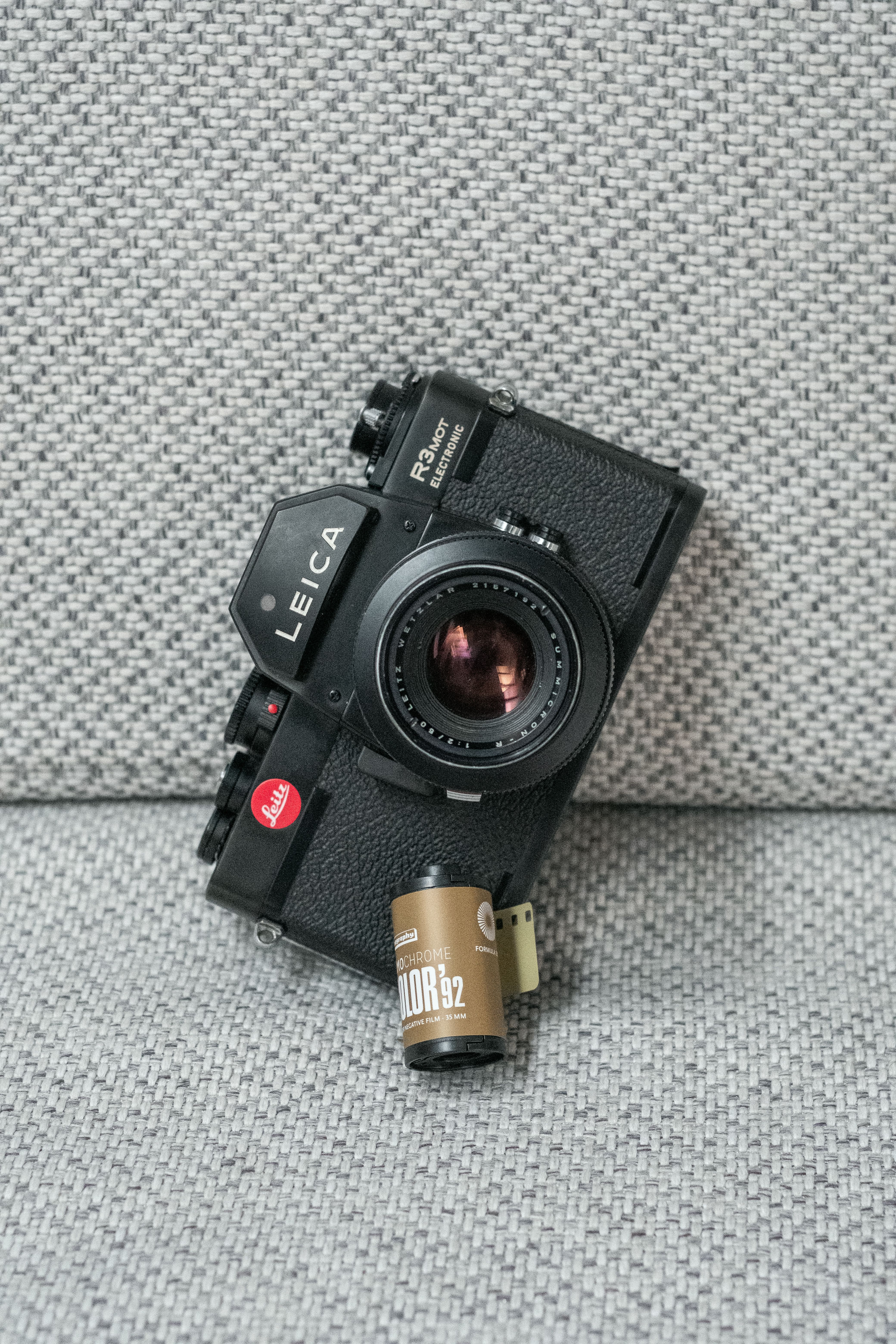 Close-up of a classic Leica R3 film camera paired with a color film roll on a textured surface.