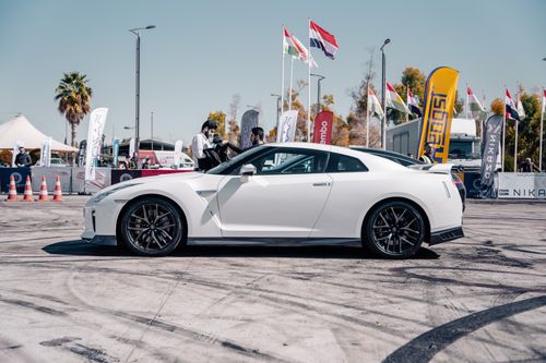 Free White Nissan GT-R at an outdoor car event, showcasing under blue skies with various flags. Stock Photo