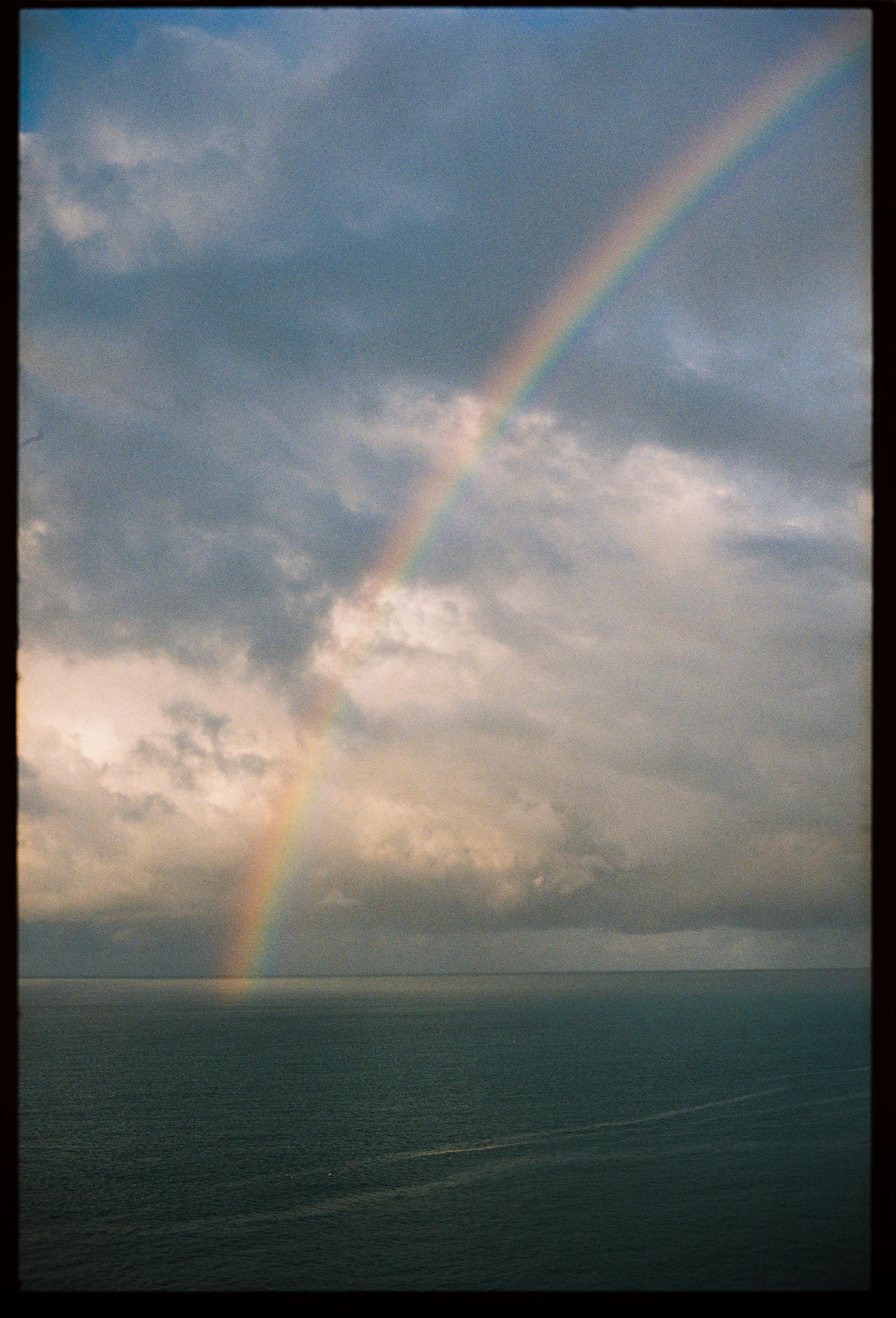 A stunning rainbow arcs over a vast ocean under dramatic cloudy skies.