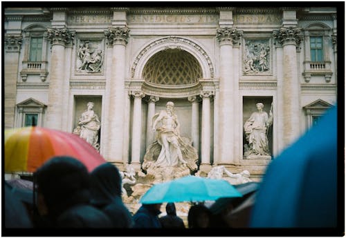 People are holding umbrellas in front of a fountain