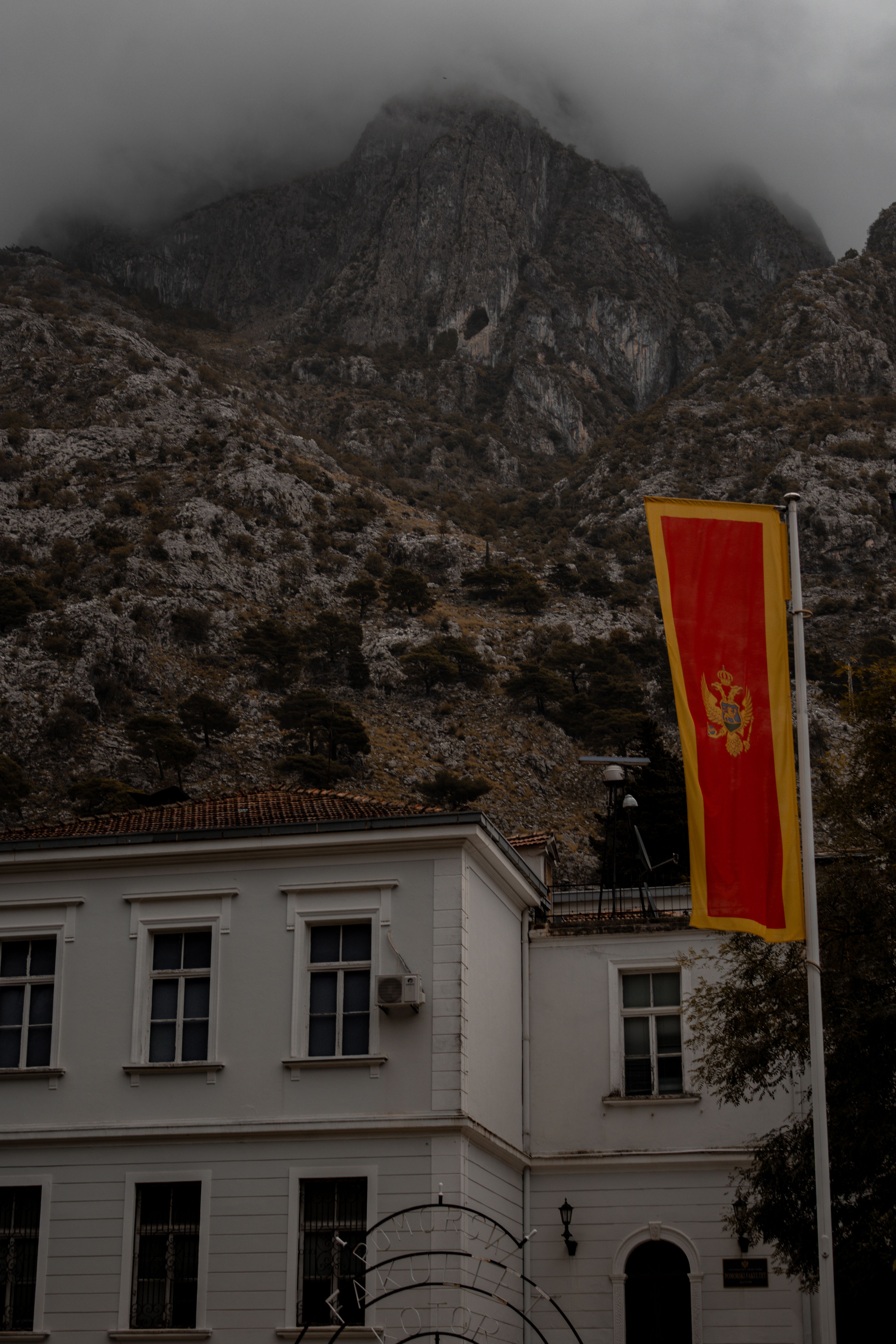 Scenic view of Montenegro flag with cloudy mountains and traditional architecture in Kotor.