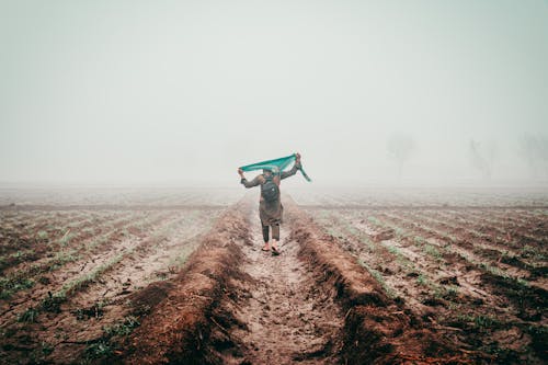 A man walking through a field with a green scarf