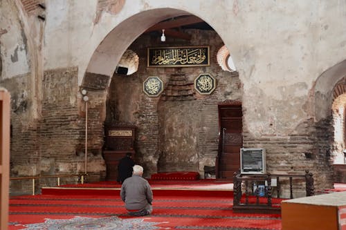 A man sitting in a mosque with a prayer rug