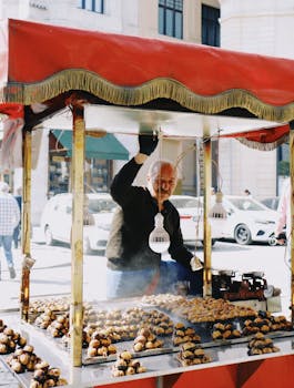 An elderly vendor selling roasted chestnuts at a street market stall with a colorful canopy.