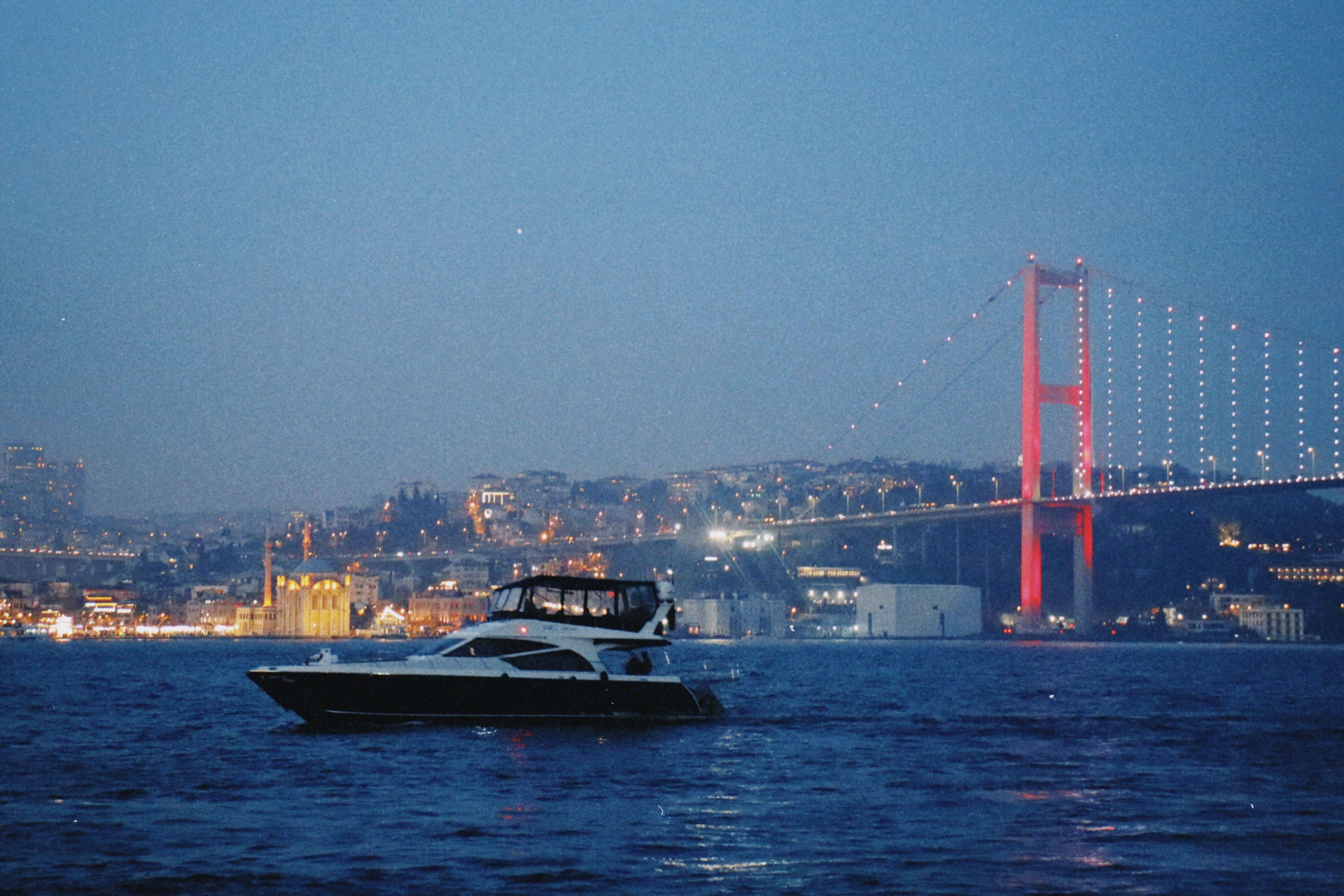 Free A yacht sails by the illuminated Bosphorus Bridge, offering a stunning Istanbul cityscape view at night. Stock Photo