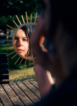 Woman looks into decorative mirror outdoors in a Lisbon park, capturing reflection and emotions.