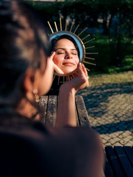 A woman with eyes closed enjoying sunlight reflection in a mirror outdoors in Lisbon.