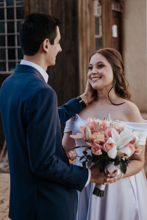 A bride and groom smile at each other in front of a building
