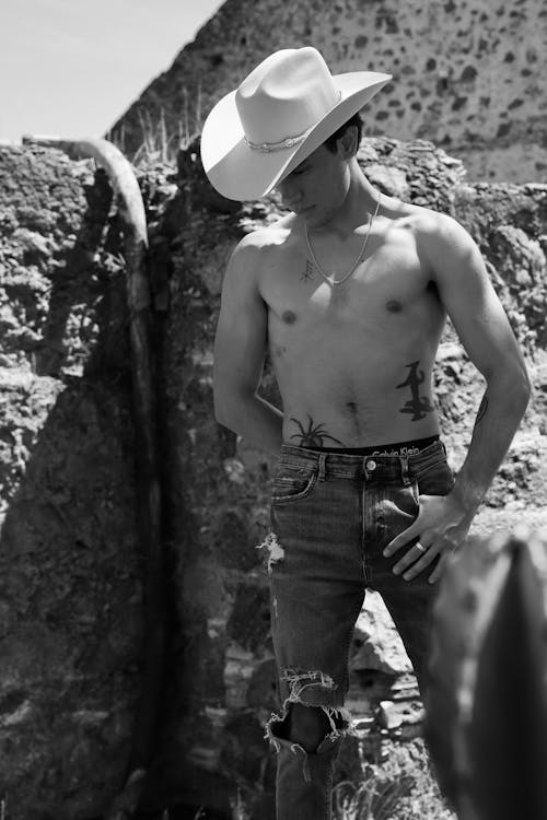A man in a cowboy hat and shirt standing next to a rock