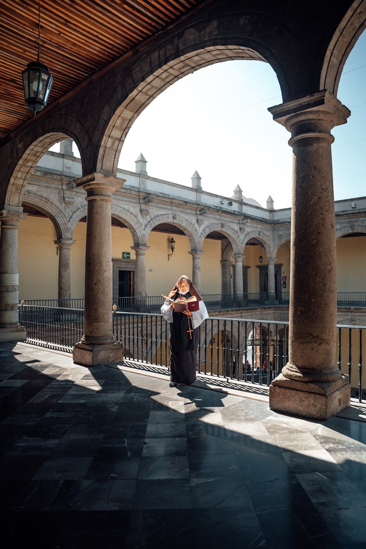 Nun Standing With Book Near Columns