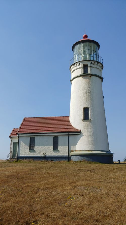Free A picturesque lighthouse stands tall under a clear blue sky on a grassy hill. Stock Photo