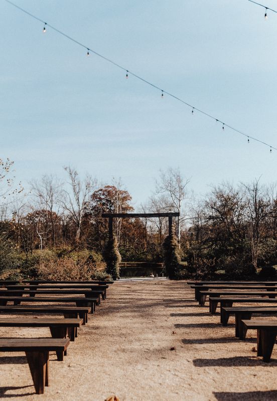 Outdoor autumn wedding ceremony venue with wooden benches, rustic arch, and fall trees in the background