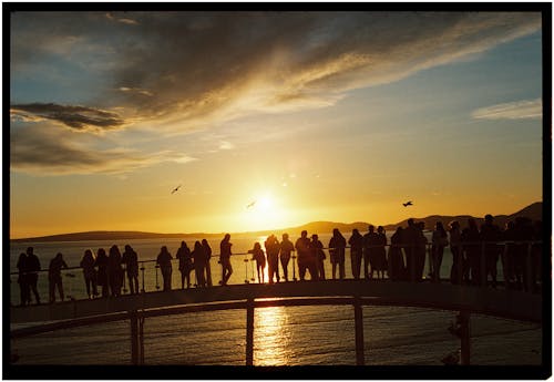 A group of people standing on a pier watching the sun set