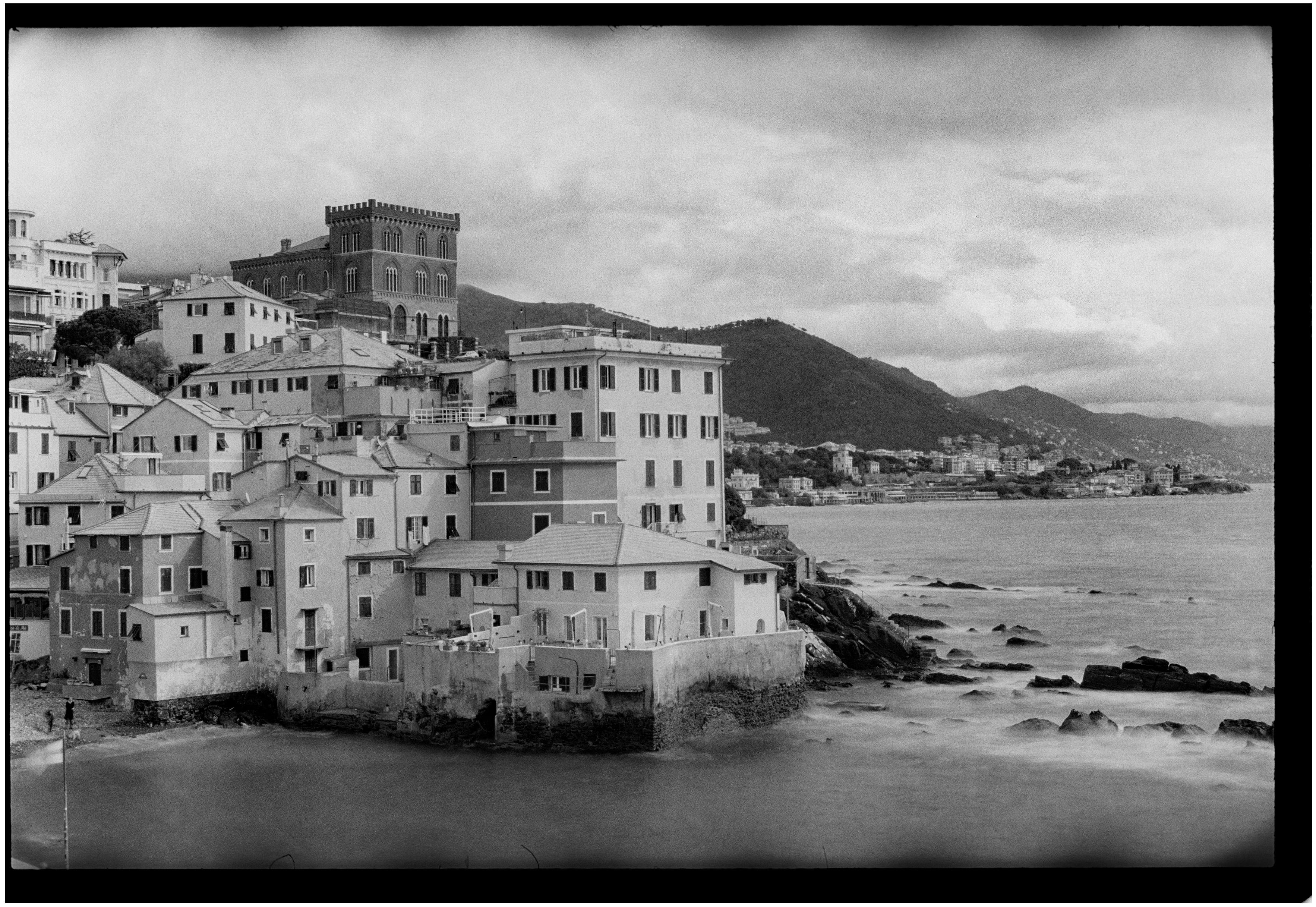 Scenic view of Genoa's coastline with historic buildings, captured in monochrome.