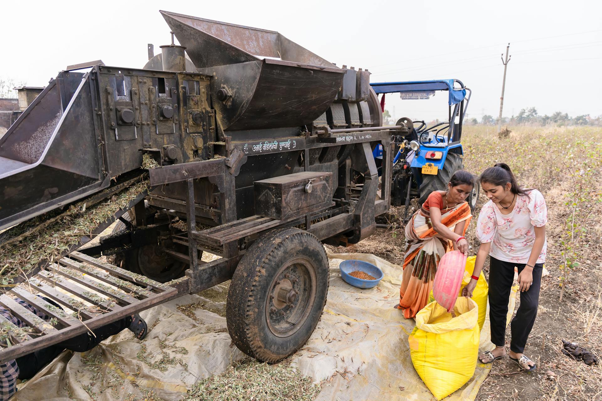 Two women packing grains using agricultural machinery in a rural field in Nagpur, India.