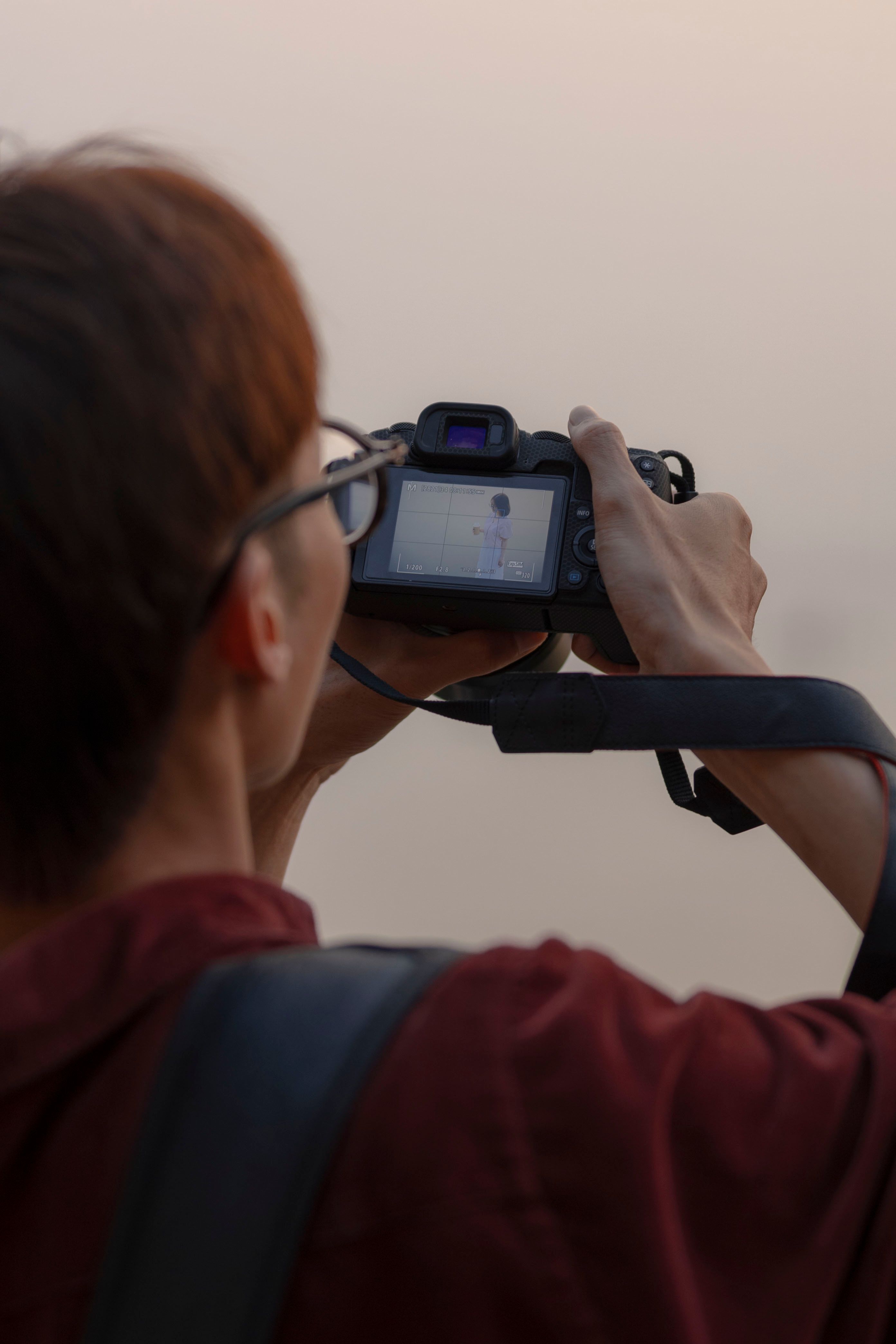 Asian man photographing with DSLR outdoors during the day.