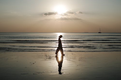 Silhouette of Woman Walking Along Seashore at Dawn