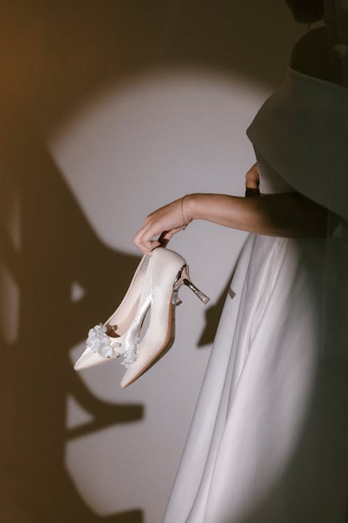 A woman in a wedding dress holding a pair of shoes
