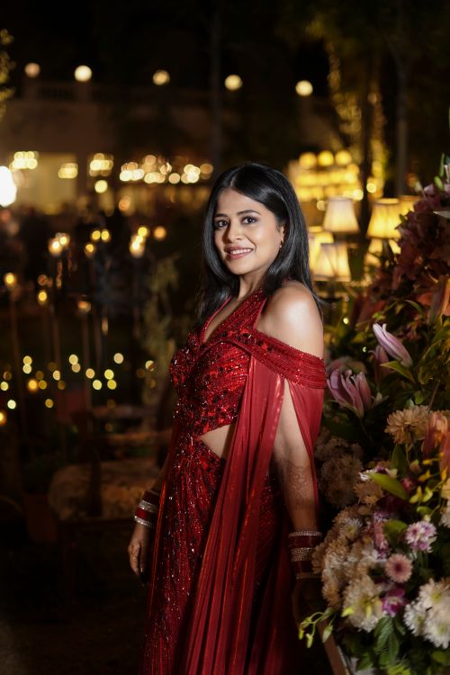 Free Smiling woman in a red dress with floral surroundings at a night event, exuding elegance and warmth. Stock Photo