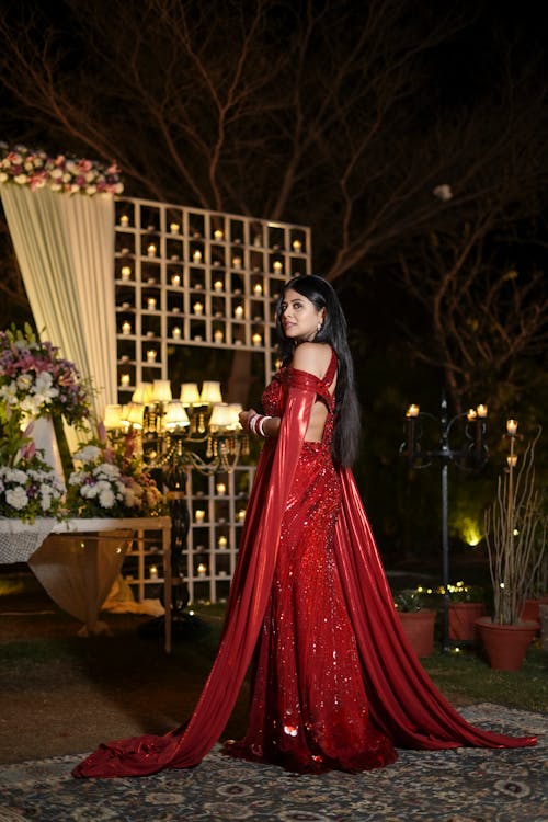 Young Woman in an Elegant Red Dress Posing in a Garden at Night 