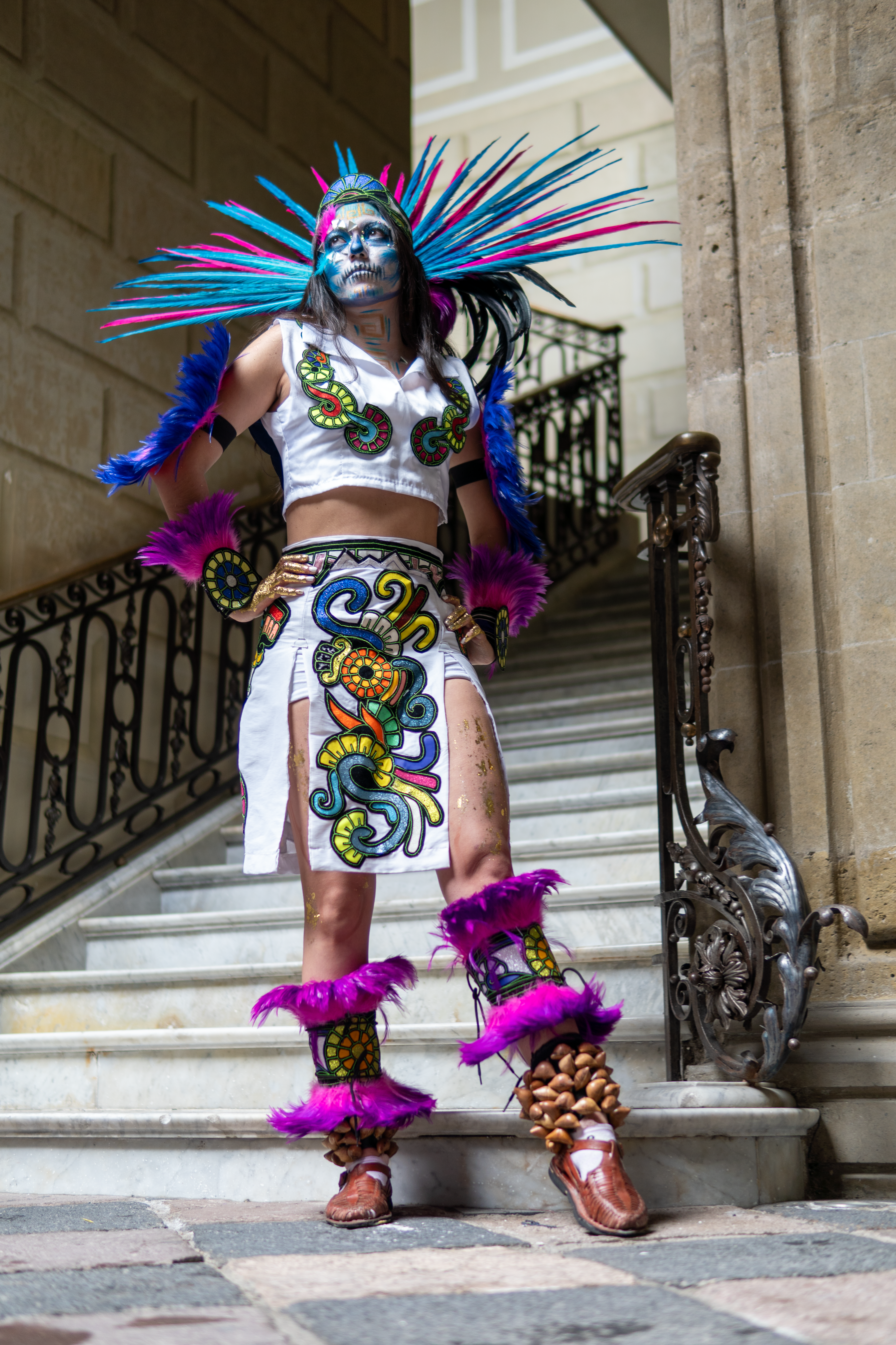 A woman in vibrant traditional Mexican attire poses on ornate stairs in Mexico City.