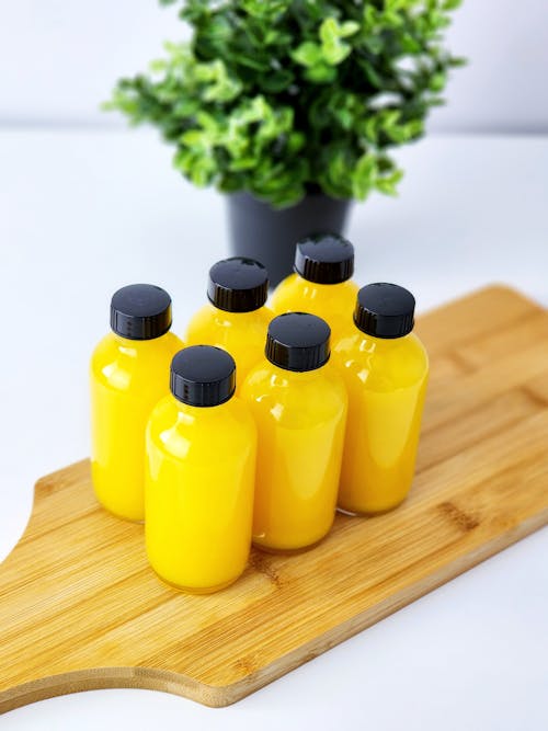 A wooden cutting board with four bottles of orange juice