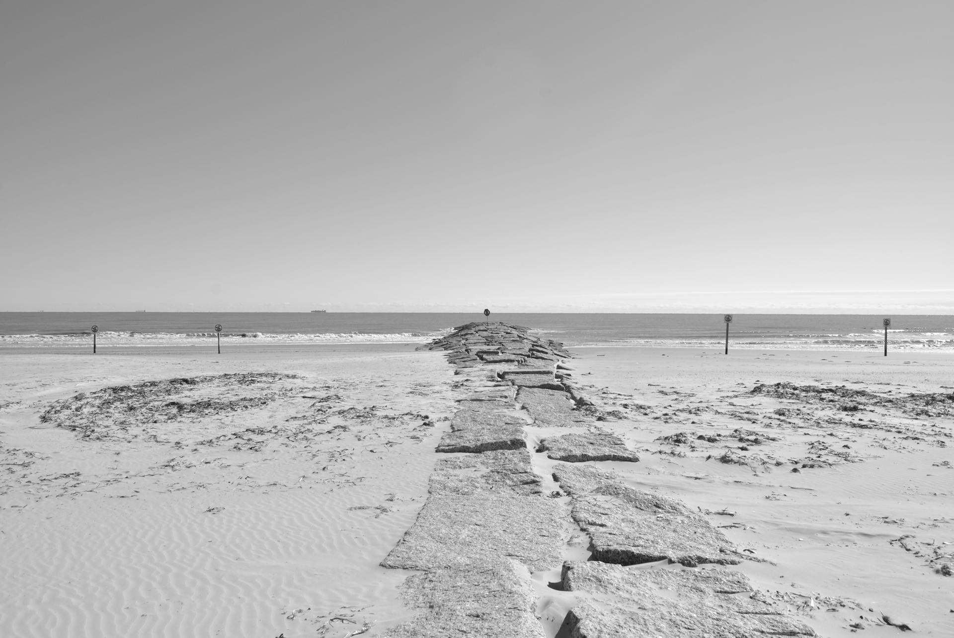Monochrome view of a stone walkway leading to the ocean at Galveston, TX beach.