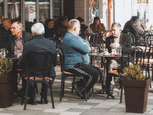 Free Senior men engaging in conversation at a bustling outdoor cafe on a city street. Stock Photo