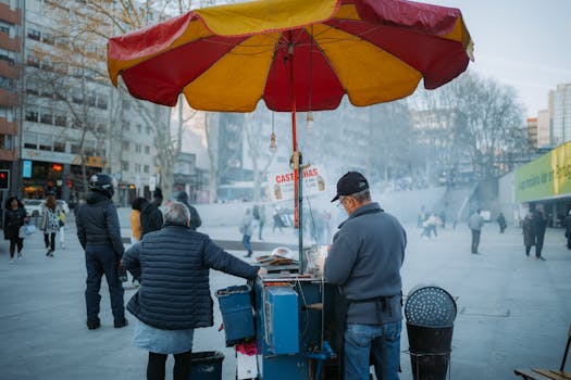A bustling urban scene with a street vendor selling roasted chestnuts under a colorful umbrella.