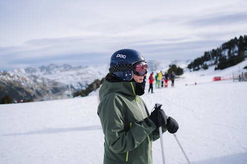A woman in a green jacket and ski gear standing on a snow covered slope