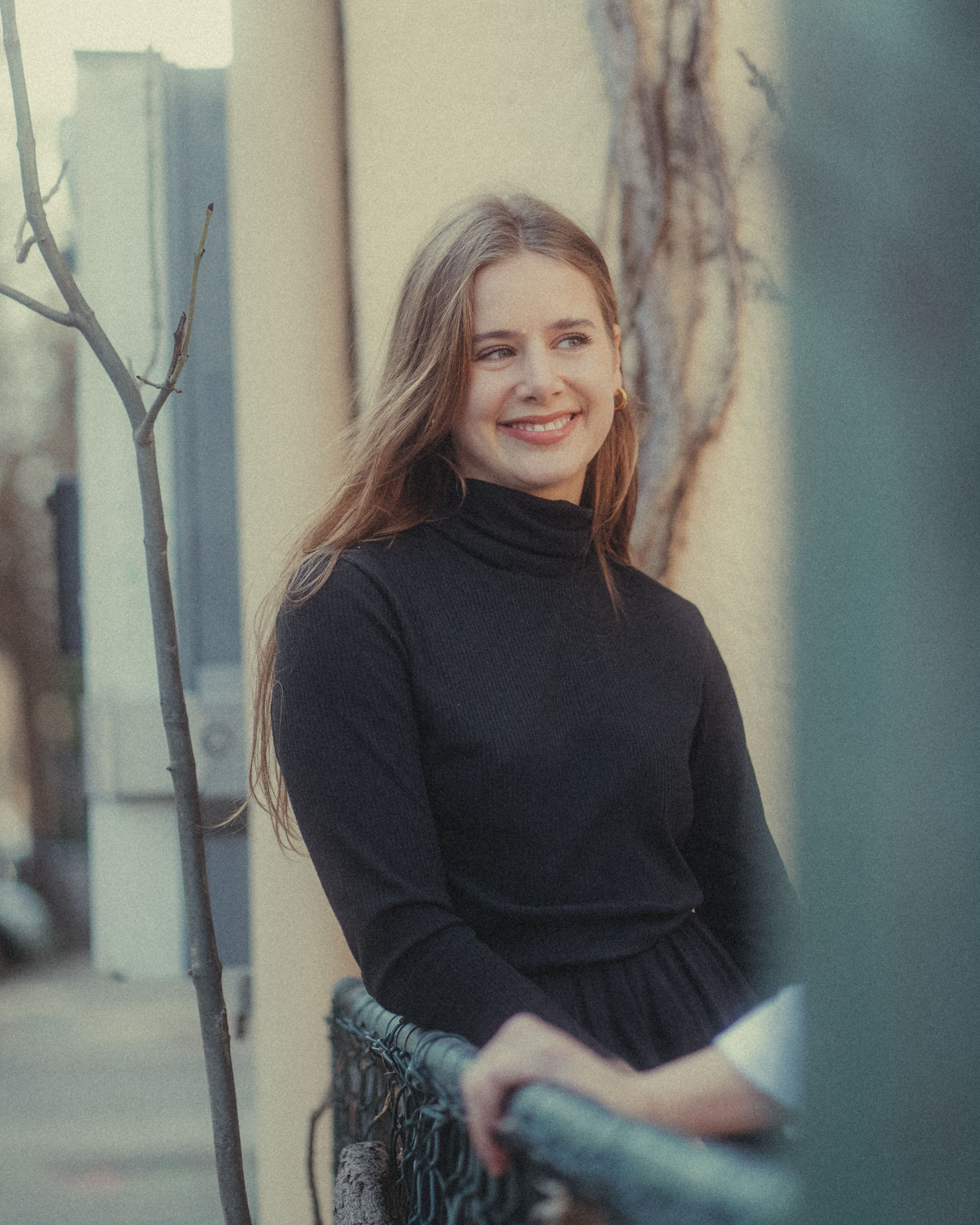 Young woman wearing a black turtleneck smiling outdoors in a casual setting.