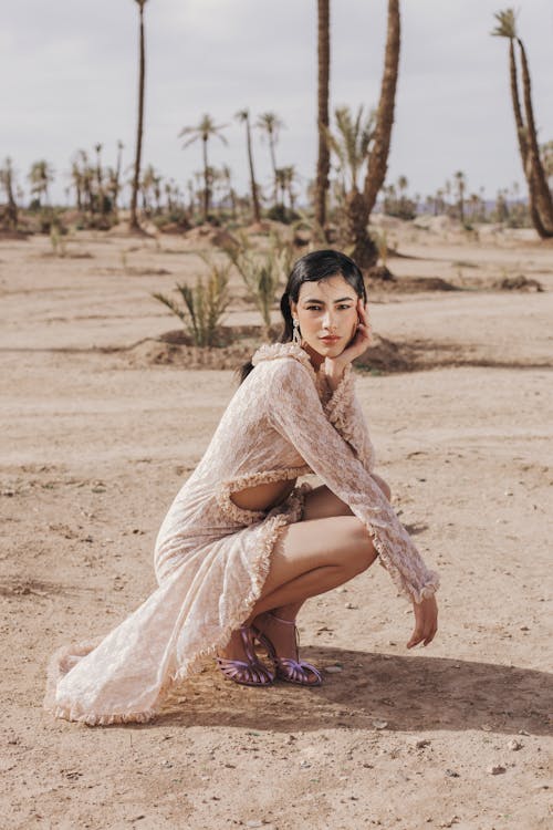 Free A woman in a dress crouches down in the desert Stock Photo
